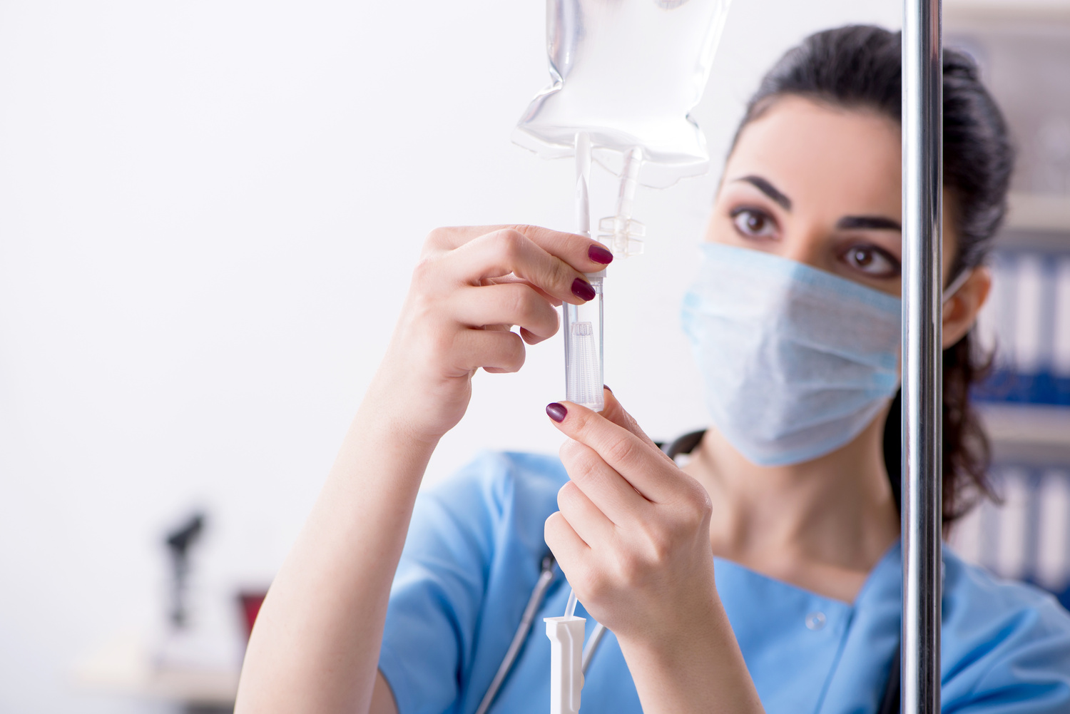Nurse adjusting and preparing an IV therapy infusion bag while wearing protective mask and gloves.
